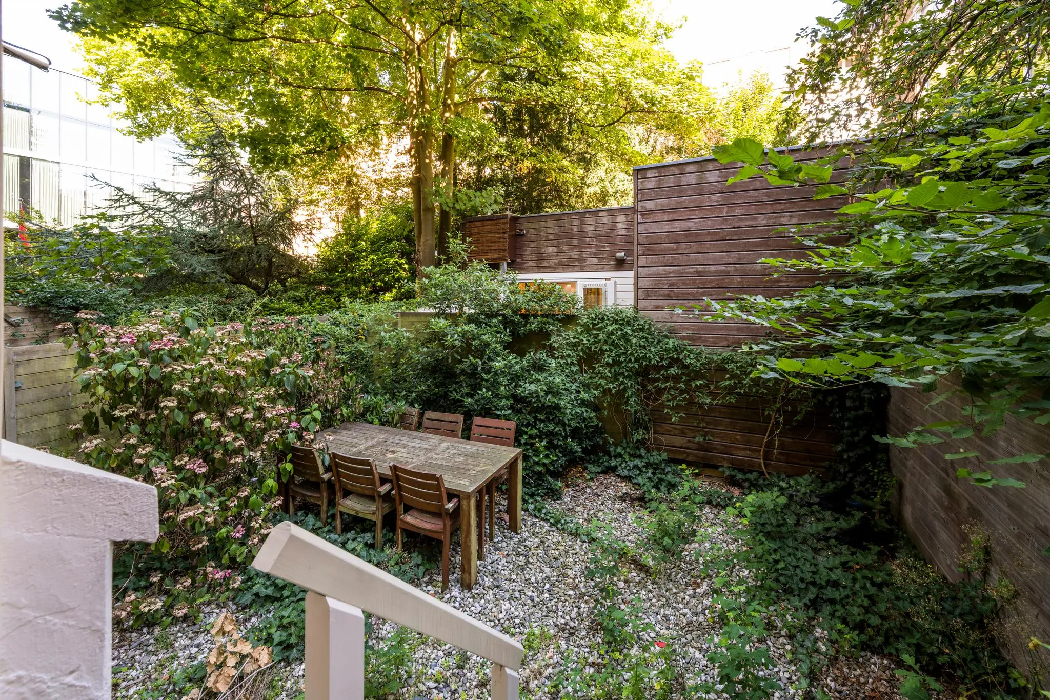 Groene stadstuin aan de Paulus Potterstraat met houten eettafel, stoelen en weelderige begroeiing.